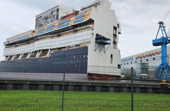 Der vorübergehend ausgedockte Mittelteil eines neuen Luxusliners im Hafenbecken vor den  Hallen der Meyer Werft.